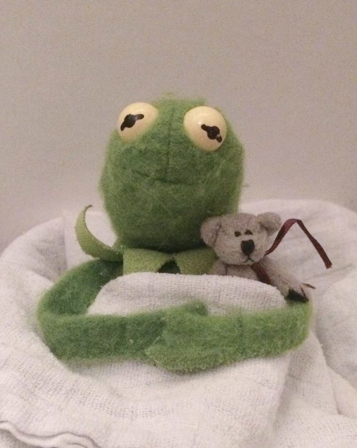 a green stuffed animal sitting on top of a white blanket