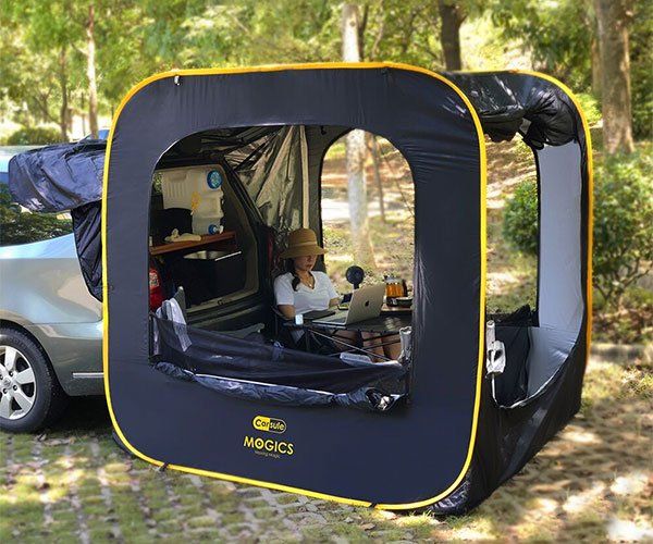 a woman sitting in the back of a car next to a tent with its door open