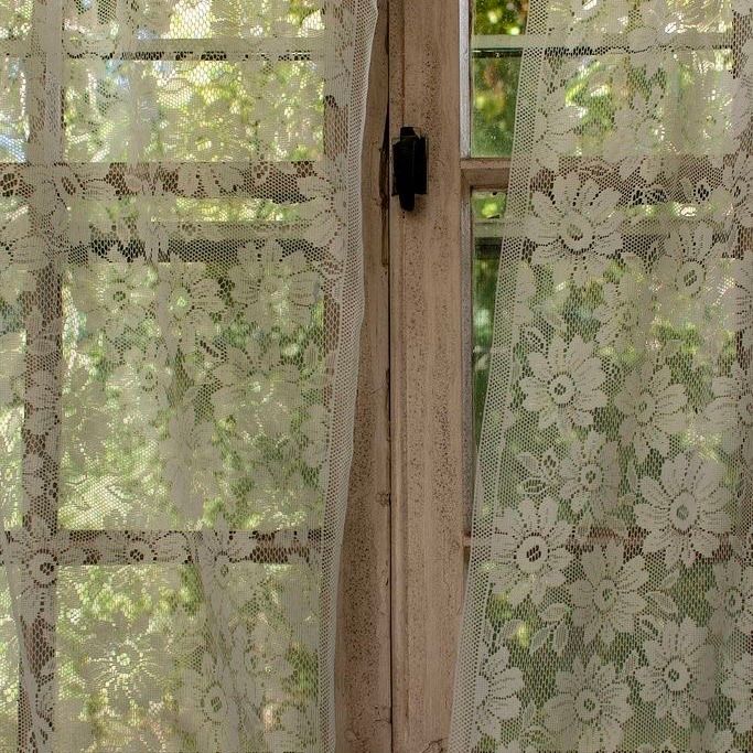 an open window with lace curtains and flowers on it