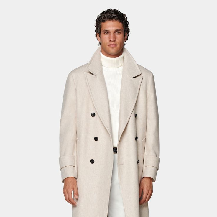 Mid-thigh length overcoat in sand, featuring wide peak lapels and natural shoulders. Double-breasted closure, patch pockets, and inside pockets for functionality. Single vent, lined, with martingale belt for style. Beige Wool Coat With Notch Lapel And Hidden Buttons, Beige Pea Coat With Notch Lapel And Hidden Buttons, Beige Single Breasted Wool Coat With Notch Lapel, Formal Single-breasted Beige Wool Coat, Luxury Cream Outerwear With Double Button Closure, Formal Beige Single-breasted Wool Coat, Luxury Beige Pea Coat With Lapel Collar, Luxury Beige Double-breasted Pea Coat, Tailored Beige Wool Coat With Hidden Buttons