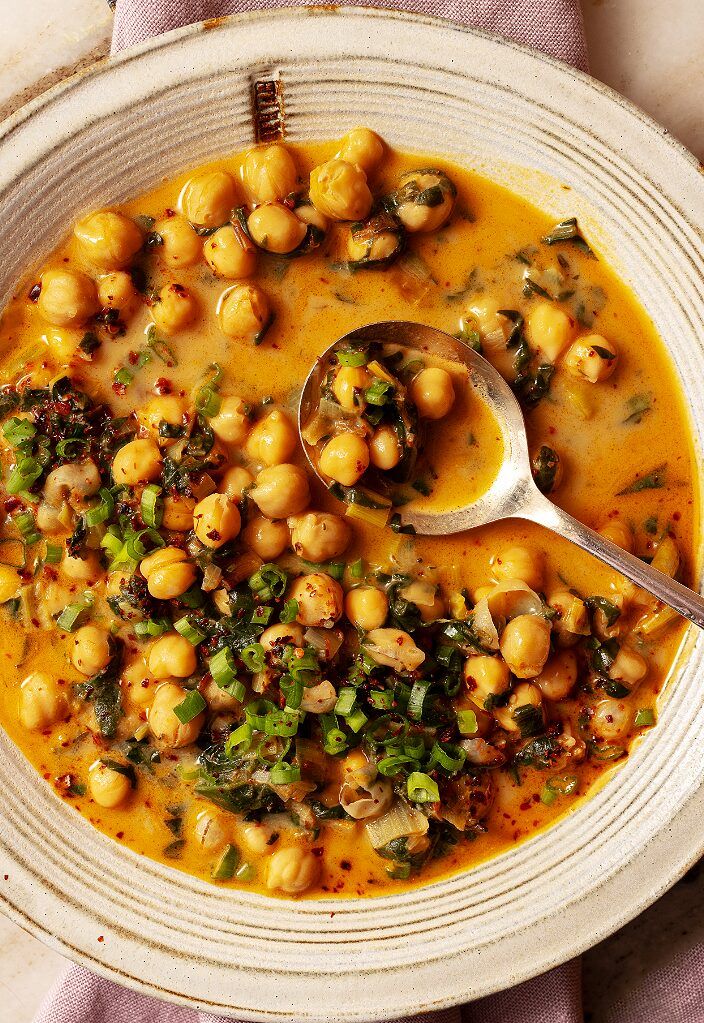 a bowl of chickpeas and spinach soup with a spoon on the side