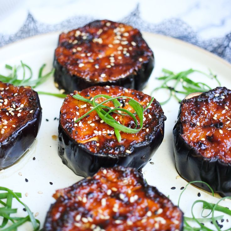 some black eggplant on a white plate topped with sesame seeds and garnish