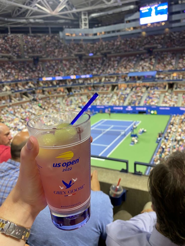 a person holding up a drink at a tennis match