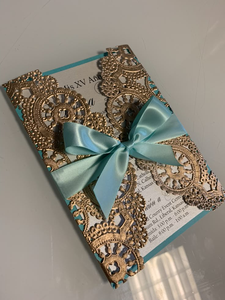 a blue and gold wedding card with a bow on it's front side, sitting on a table