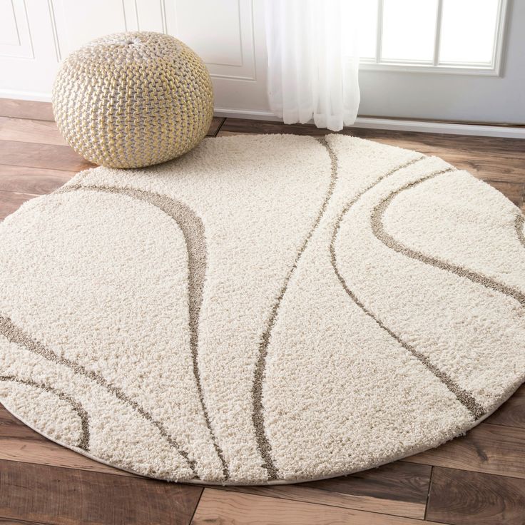 a white rug with an abstract design on the floor next to a round ottoman in a living room