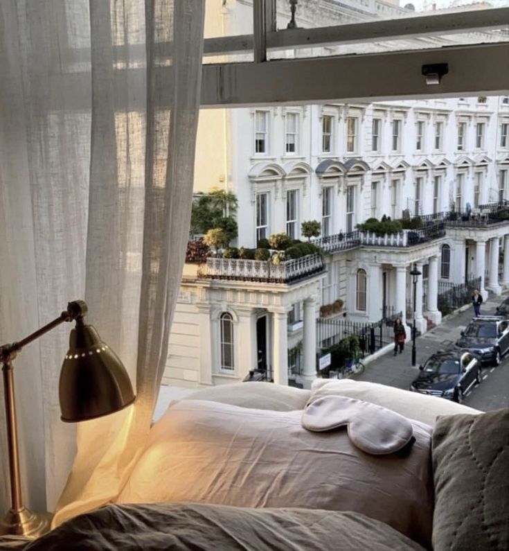 a bed sitting in front of a window next to a tall white building with lots of windows