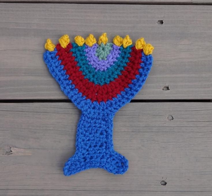 a crocheted blue vase with yellow flowers on it sitting on a wooden surface