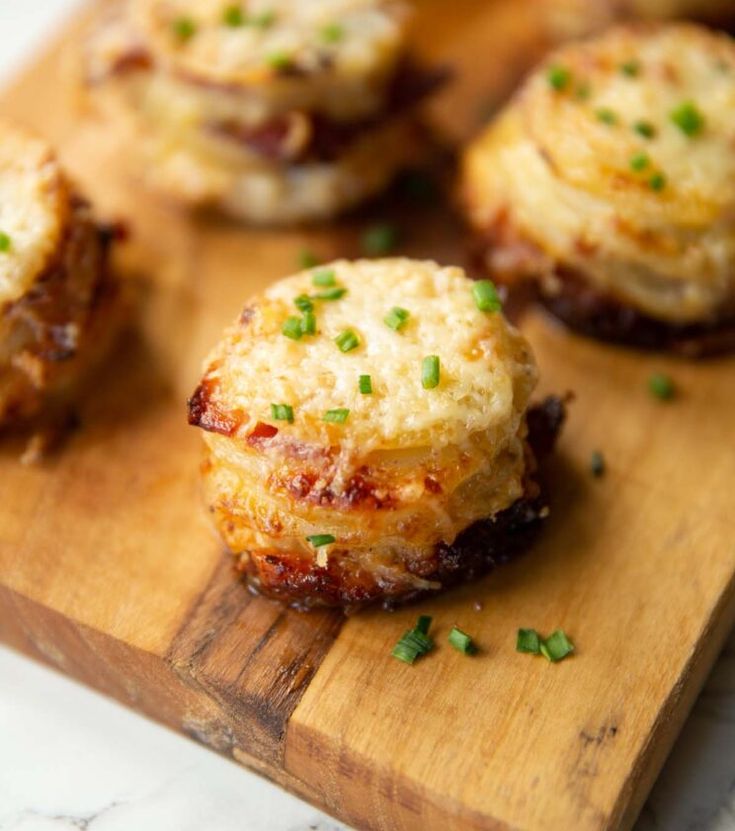 mini pizzas on a wooden cutting board topped with cheese and chives