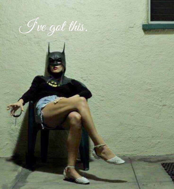 black and white photograph of a woman wearing a batman mask sitting on a chair in front of a wall