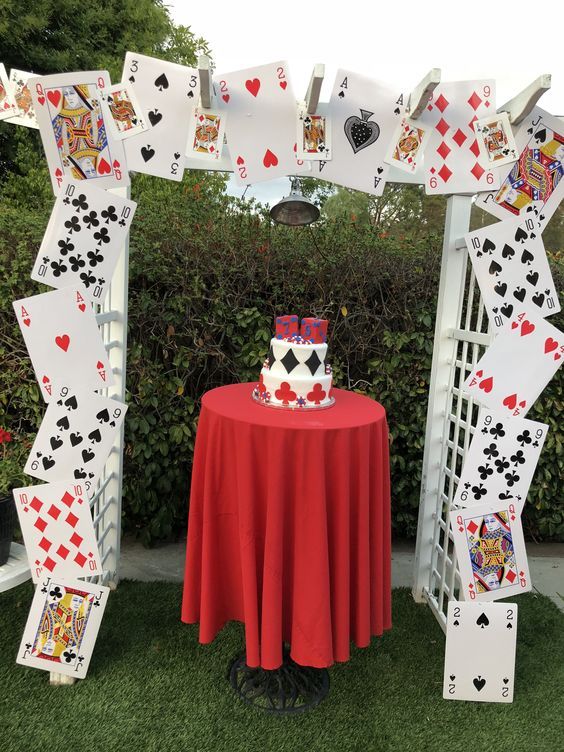 a red table topped with a cake covered in playing cards on top of a lush green field