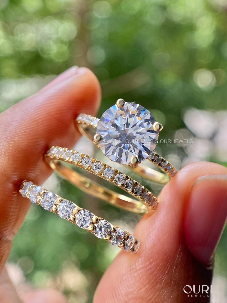 a woman's hand holding two gold rings and a diamond ring in her left hand