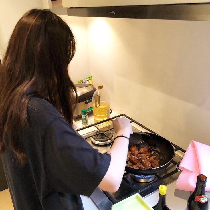 a woman cooking food in a pan on top of a gas stove next to a bottle of beer