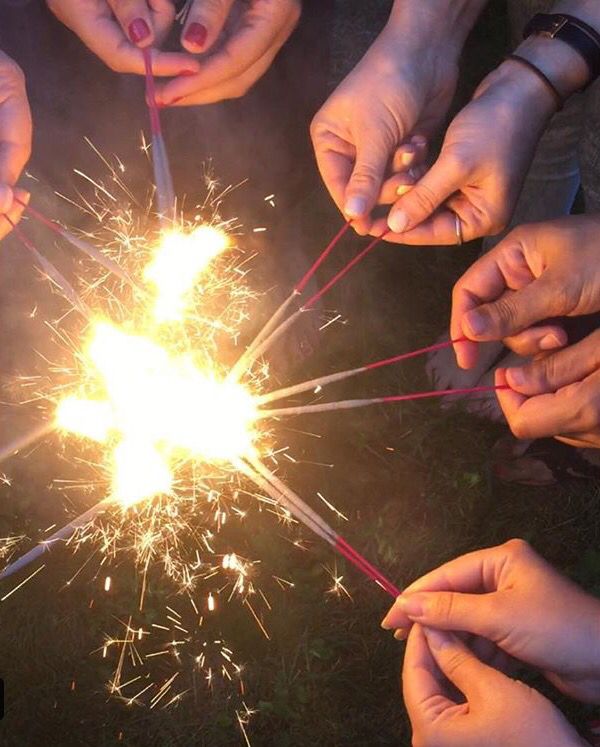 several people holding sparklers in their hands over a firework display on the ground