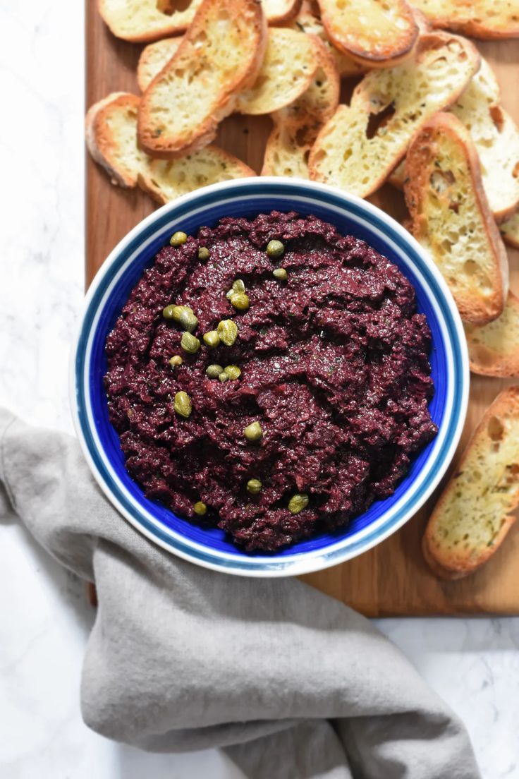 a blue bowl filled with food on top of a wooden cutting board next to slices of bread