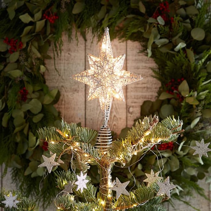 a small christmas tree with lights on it in front of a wooden wall and wreath