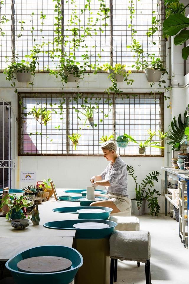 a woman standing at a counter in a room filled with potted plants