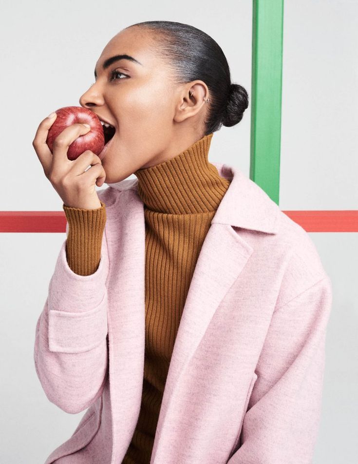 a woman in a pink coat eating an apple