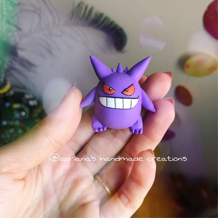 a hand holding a purple toy with an evil smile on it's face and eyes