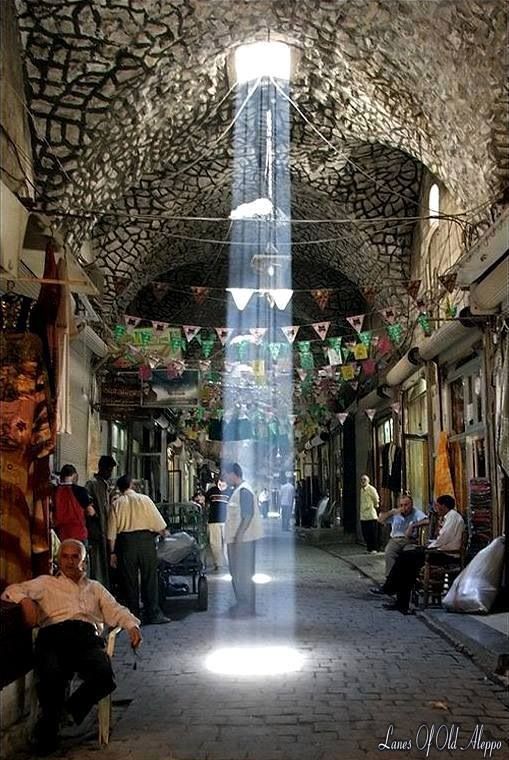 people are sitting on benches in an alleyway with lights coming from the ceiling and hanging decorations