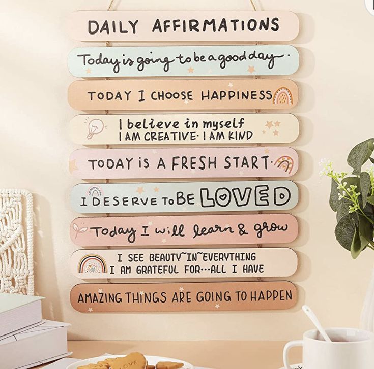 a wooden sign that says daily affirmations hanging on a wall next to a cup of coffee