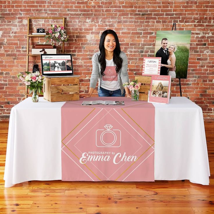 a woman standing behind a table with photos on it and an emo sign in front of her