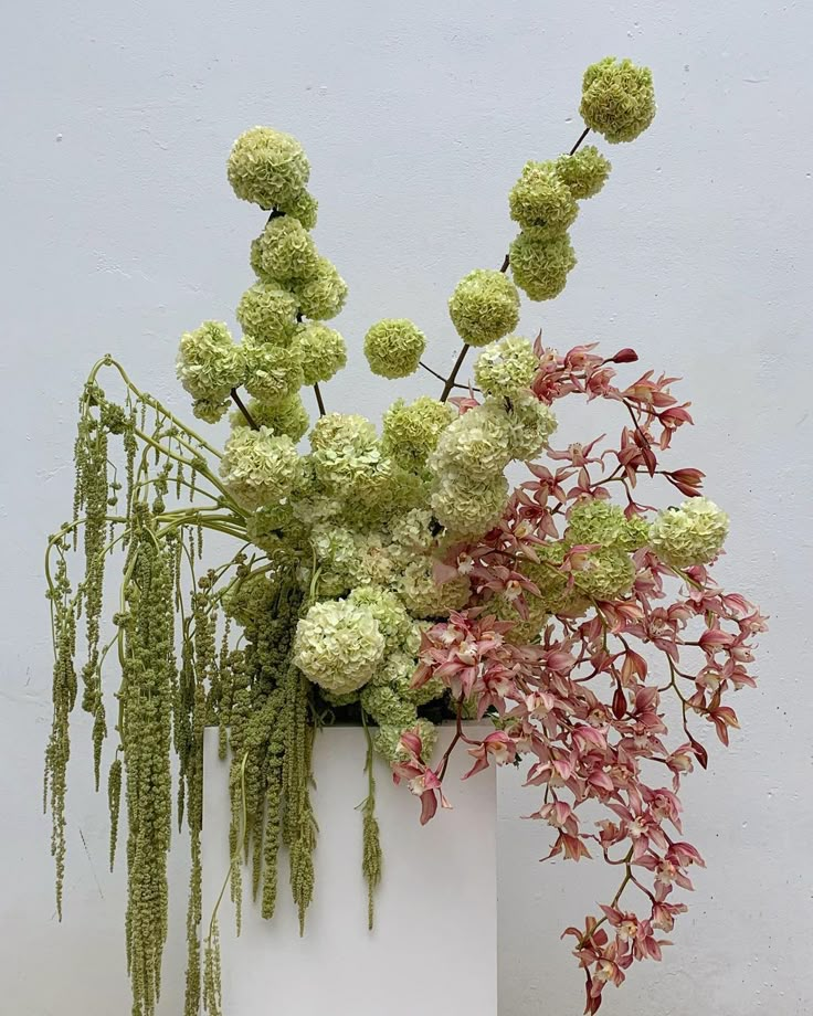 a white vase filled with lots of green and pink flowers