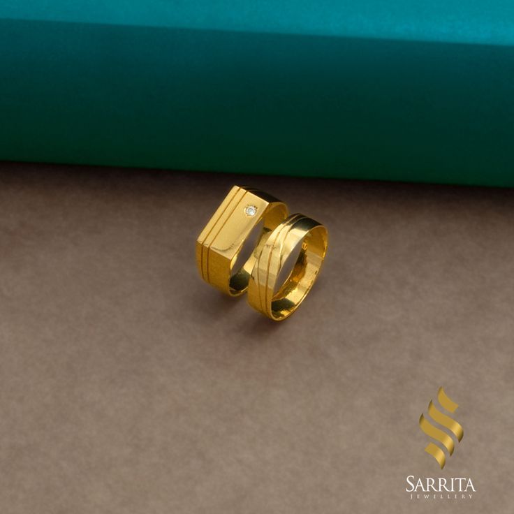 two gold rings sitting next to each other on top of a brown surface with a green background