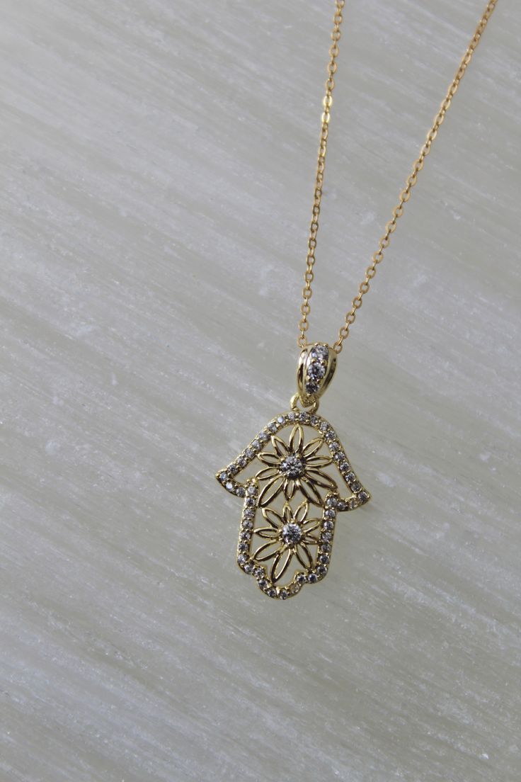 14k gold filled chain 14k gold filled floral hands pendant with CZ stones Introducing our Unique Gold Filled Floral Hamsa Necklace, a captivating blend of elegance and tradition. This beautiful necklace features an intricately designed Hamsa pendant adorned with delicate floral patterns and sparkling stones. Crafted from high-quality gold filled material, it offers a luxurious look and exceptional durability. The Hamsa symbol is believed to bring protection, happiness, and good fortune, making t Gold Flower-shaped Necklace With Cubic Zirconia, Gold Flower Necklace With Cubic Zirconia, Gold Flower-shaped Cubic Zirconia Necklaces, Gold Flower Pendant Jewelry With Cubic Zirconia, Gold Cubic Zirconia Flower Pendant Jewelry, Gold Flower-shaped Necklace With Diamond Accents, Gold Necklace With Diamond Accents And Flower Shape, Gold Necklace With Diamond Accents In Flower Shape, Delicate Gold Charm Necklace With Cubic Zirconia