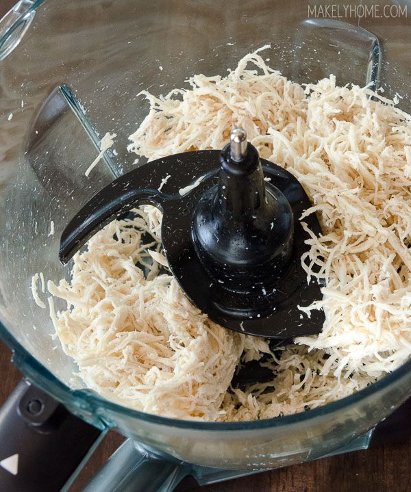 shredded cheese in a food processor with a black lid on a wooden table top, ready to be blended