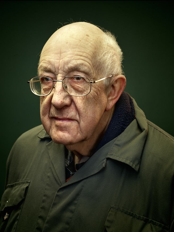 an old man wearing glasses and a green jacket looks at the camera while posing for a portrait