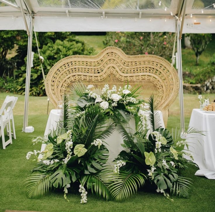 an arrangement of flowers and greenery on the grass under a canopy at a wedding