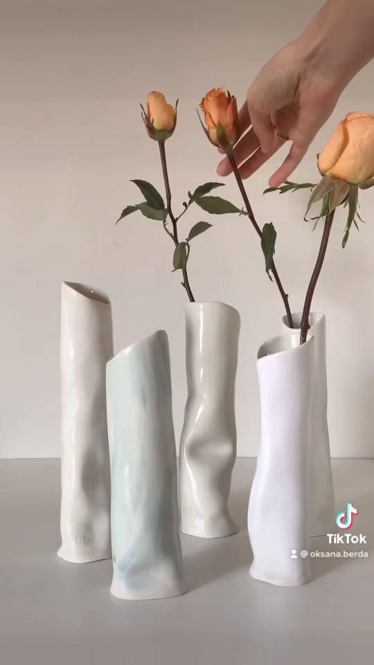 three white vases with roses in them and one being held by someone's hand