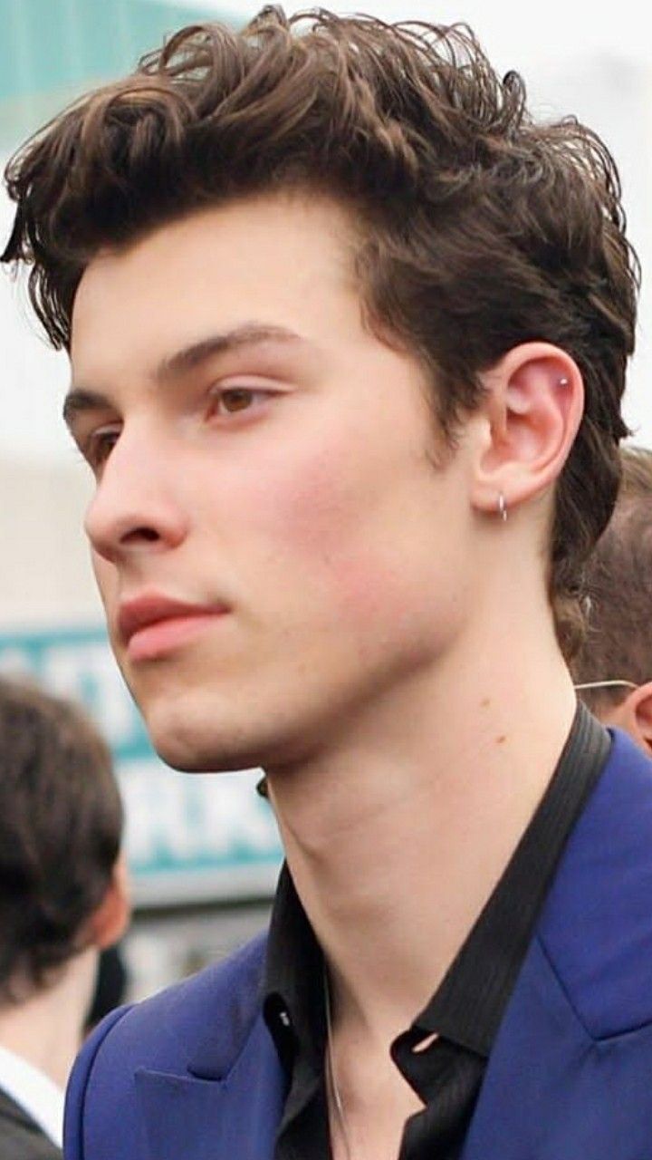 a close up of a person wearing a blue suit and black shirt with ear rings