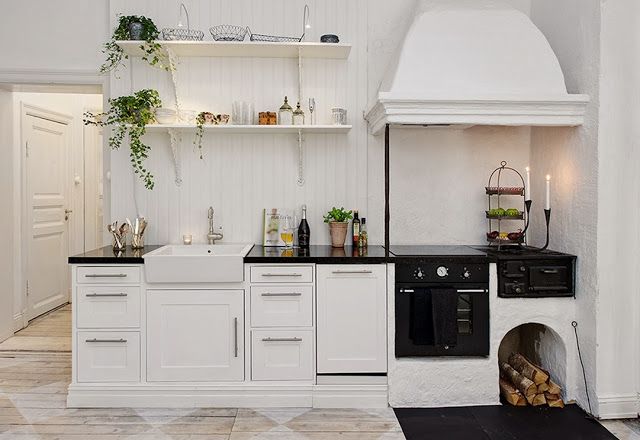 a kitchen with white cabinets and black counter tops is pictured in this image, there are plants on the shelves above the stove