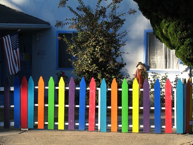 a rainbow colored picket fence in front of a house