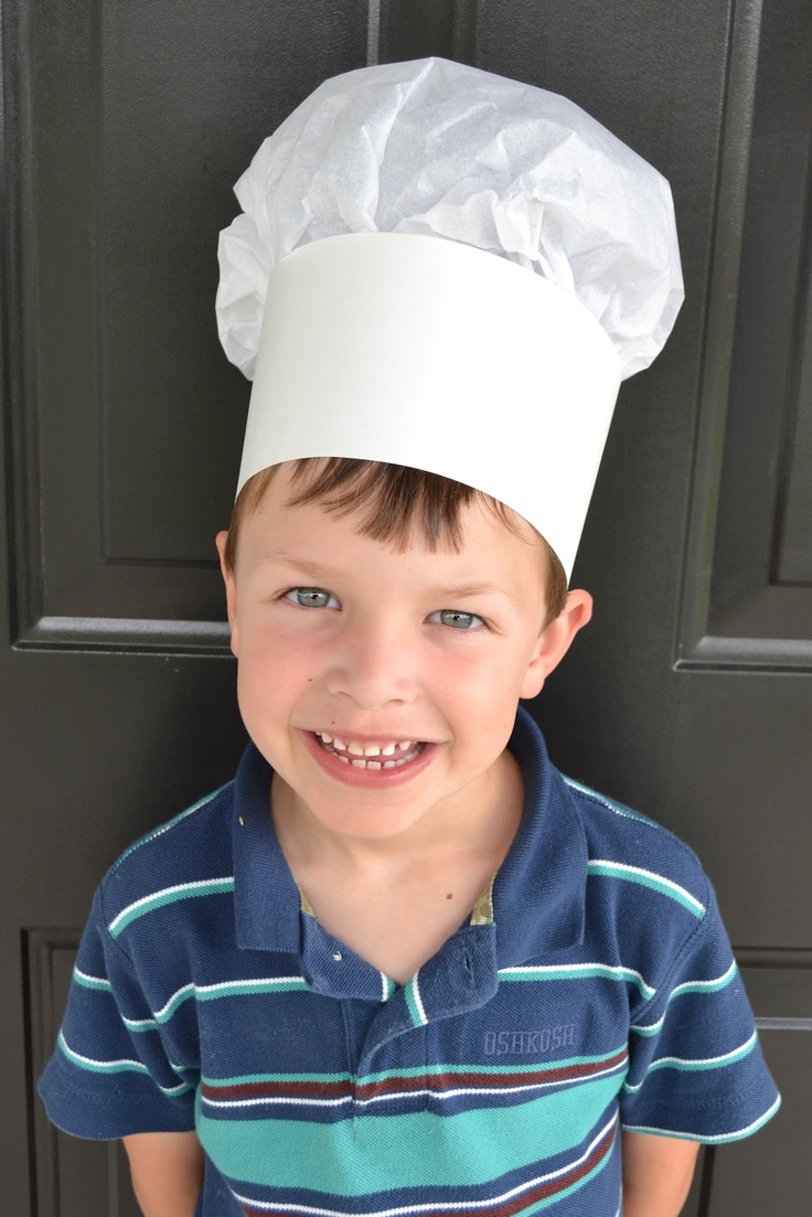 a young boy wearing a chef's hat on top of his head, standing in front of a door