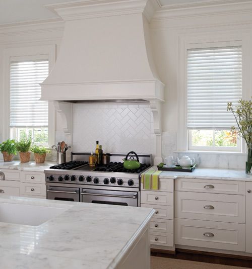 a kitchen with white cabinets and marble counter tops is pictured in this image, there are two windows above the stove