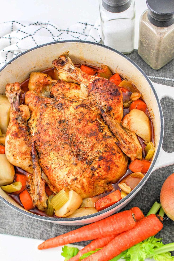 a chicken and carrots in a skillet on a table with other vegetables next to it