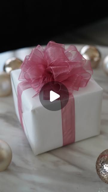 a white gift box with a pink bow on it sitting on a marble table next to ornaments