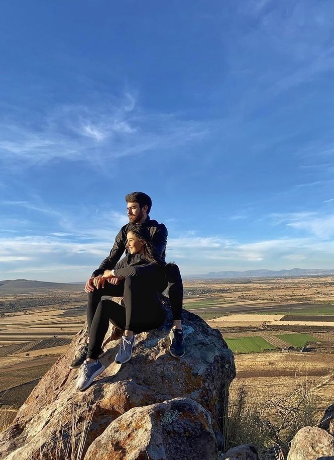 a man and woman sitting on top of a large rock in the middle of nowhere