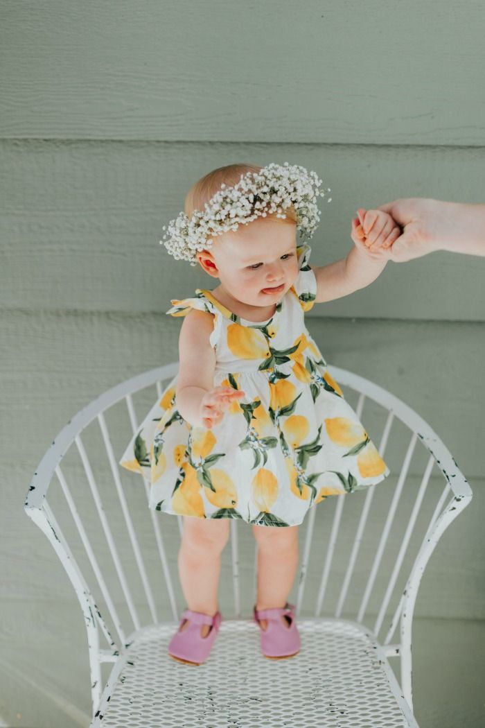 a baby girl standing on top of a white chair next to a person's hand