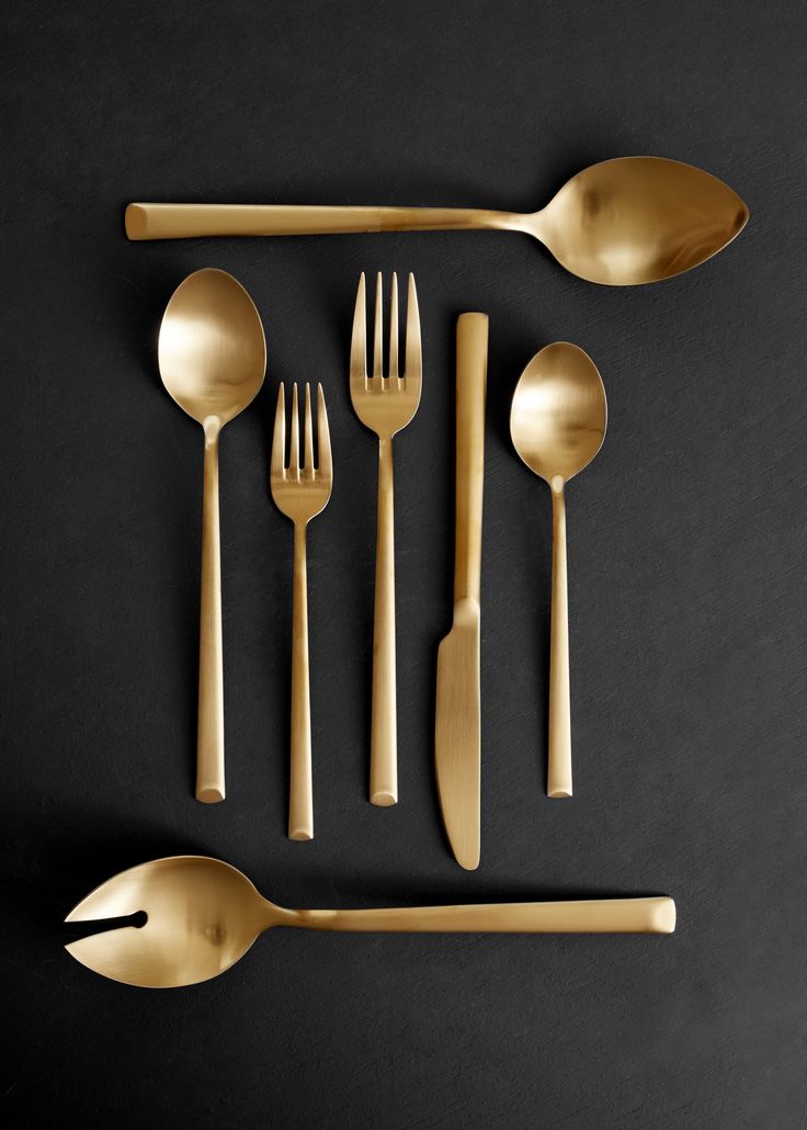 gold flatware is laid out on a black surface with spoons, forks and knives