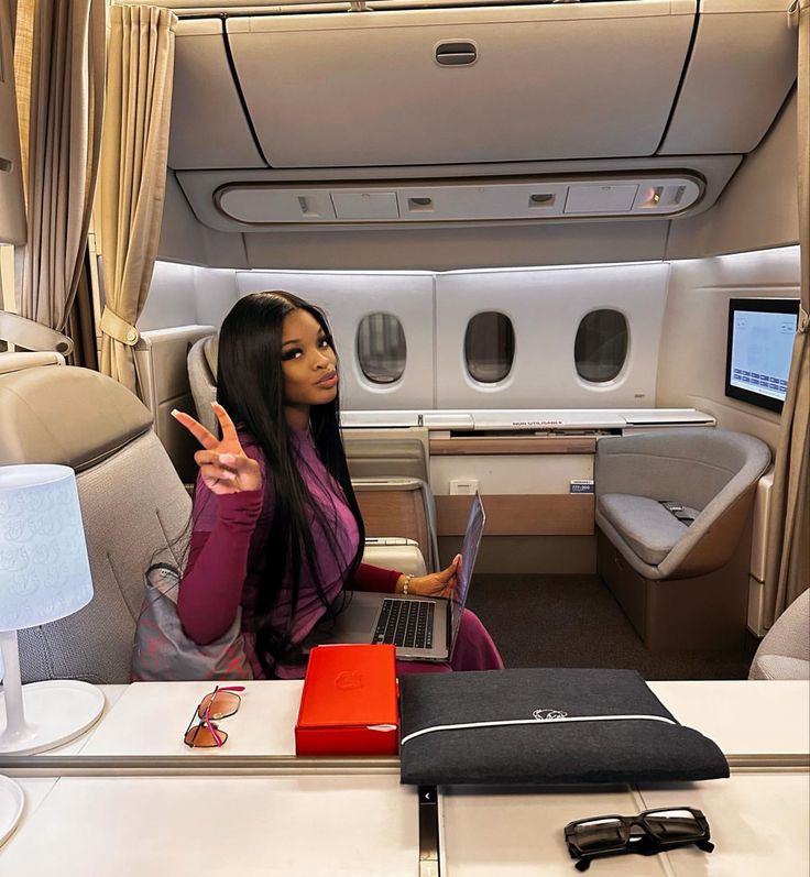 a woman is sitting in an airplane and pointing at the laptop on her lap top