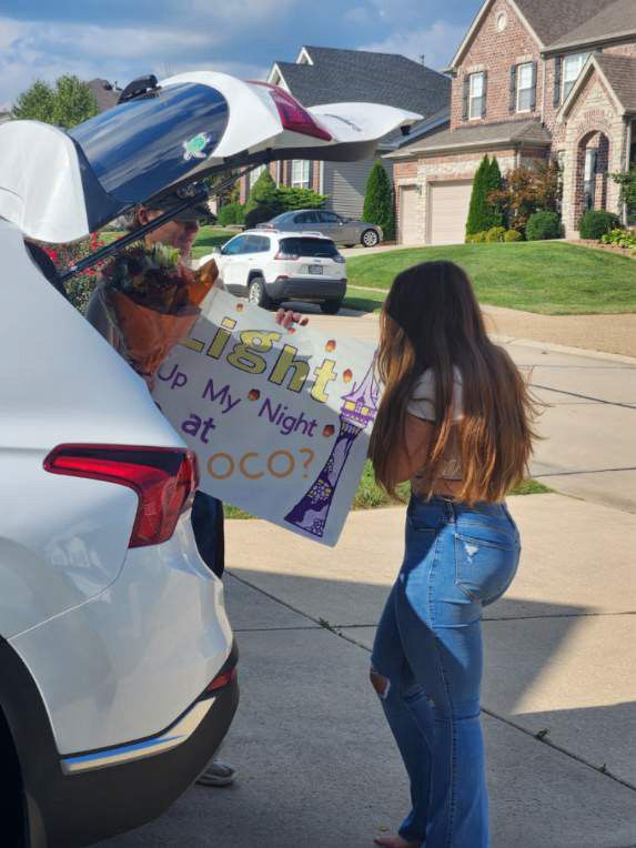 a girl standing next to a parked car holding a sign that says hush my night at noon