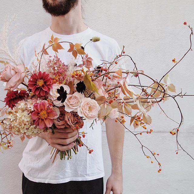 a man holding a bouquet of flowers in front of his face and wearing a white t - shirt