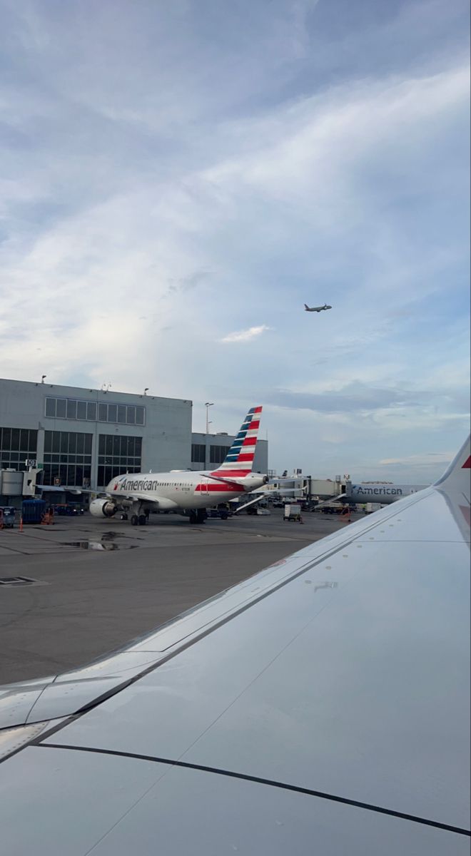 an airplane that is flying in the sky near another plane on the tarmac at an airport