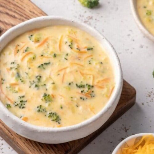 broccoli and cheese soup in a white bowl on a wooden cutting board next to other dishes