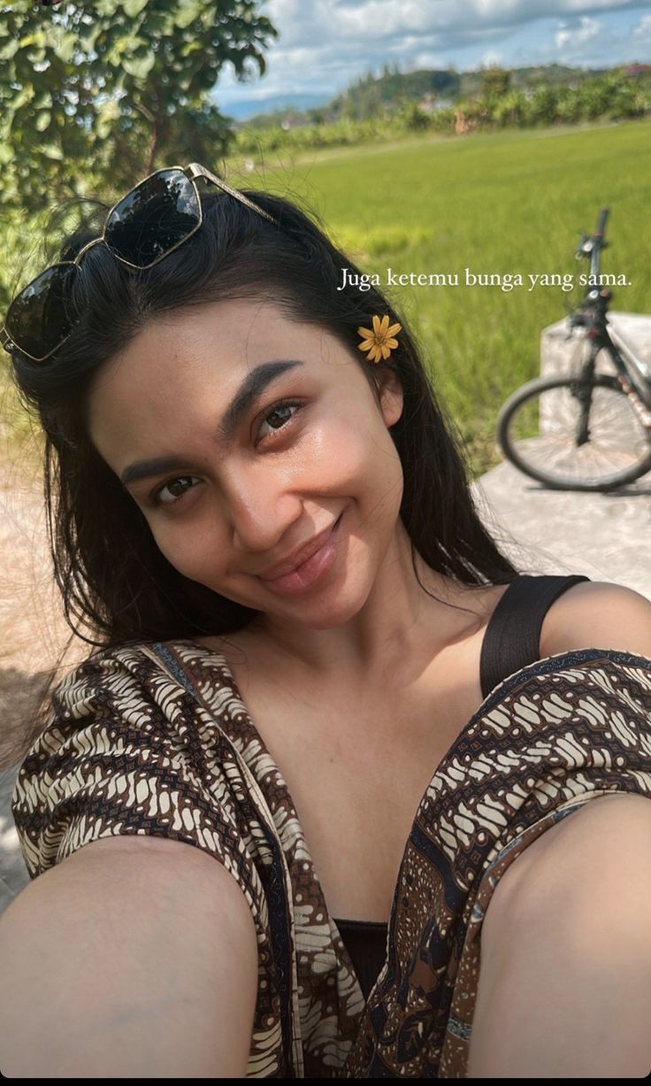 a woman taking a selfie with her bike in the background and grass behind her