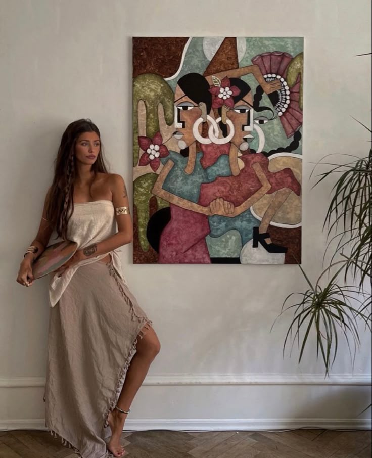 a woman standing in front of a painting on the wall next to a potted plant