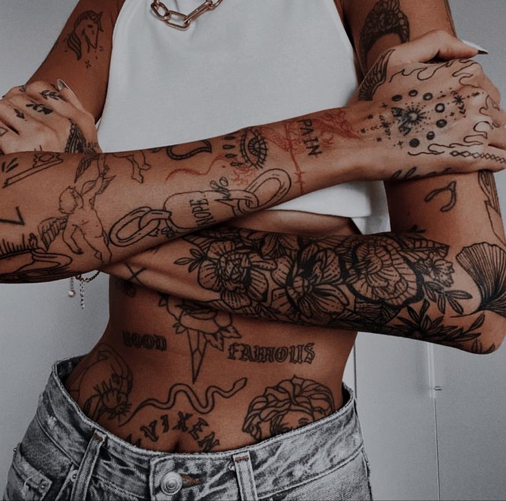 a woman with many tattoos on her arms and chest is standing in front of a white wall